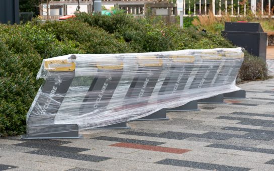 Yellow and grey cycle Hire docks on University of Salford campus wrapped in plastic film. On the side it says 'Cycle Hire' with a bee symbol