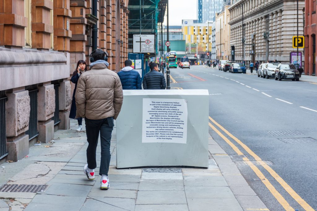 A pedestrian passing by a grey box with the official notice on it.