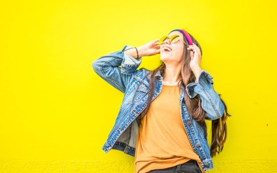 woman in sunglasses looking up smiling against yellow wall