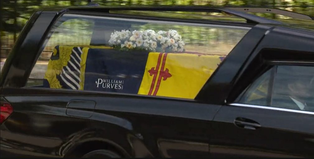 Queen Elizabeth's coffin wrapped in the Royal Standard of Scotland with a wreath of her favourite flowers from the Balmoral estate. Via Player.