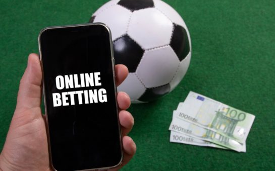 A phone with "online betting" on the screen with money and a football in the background