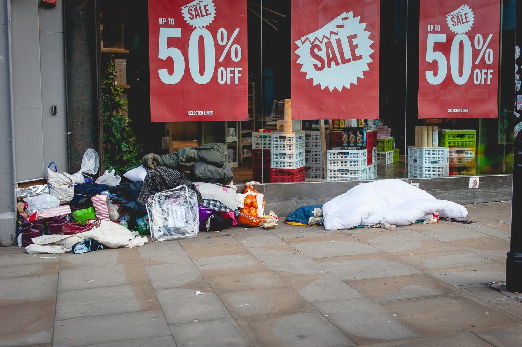 A stock photo of a homeless individual asleep on the street, next to a pile of belongings