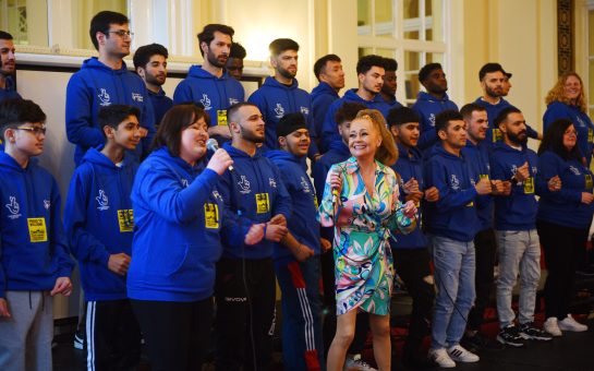 A choir in blue hoodies with two lead singers in front of them
