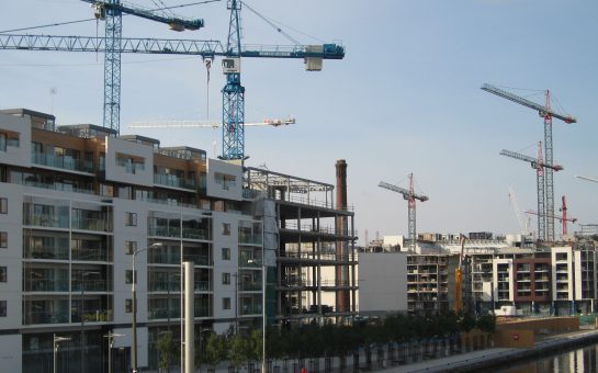 Several cranes hang over a series of apartment and office blocks. The river Liffy is visible in the bottom right corner