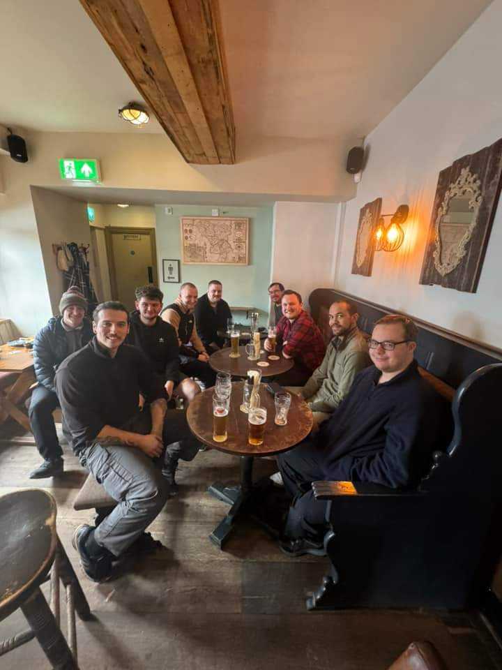 Group of men smiling at camera sat around tables in a pub