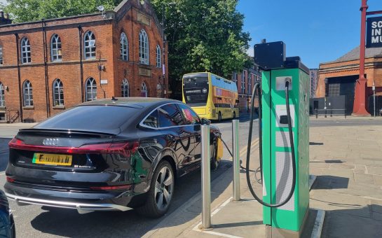 A black car is plugged into a public electric vehicle charger.