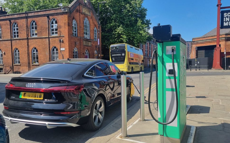 A black car is plugged into a public electric vehicle charger.