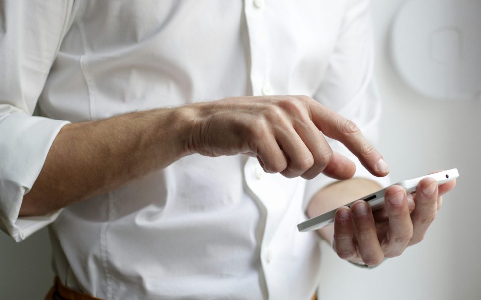 A person holding a white Android smartphone in white shirt (Credit: Free to use from Unsplash)