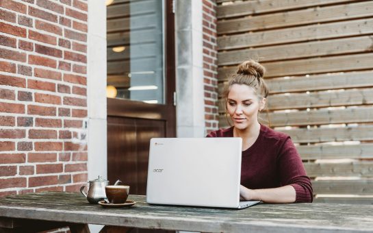 Woman sitting and holding white Acer laptop near brown wooden wall (Credit: Anete Lūsiņa/Unsplash)