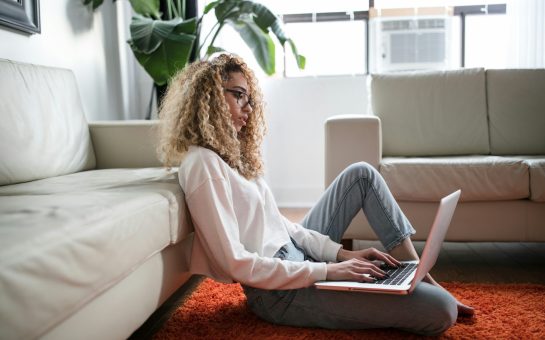 Woman sitting on floor and leaning on couch using laptop (Credit: Free to use from Thought Catalog/Unsplash)