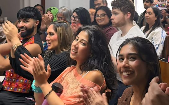 An image of the audience at the SamajhMyGal open mic event. The audience are clapping with some members of the audience looking at the camera.