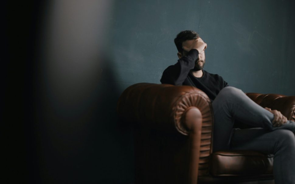 Man holding head while sitting in armchair
